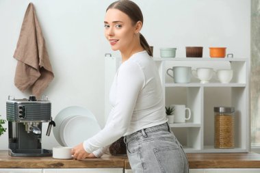 Mutfakta bir fincan sıcak kahve ve modern kahve makinesiyle güzel genç bir kadın.