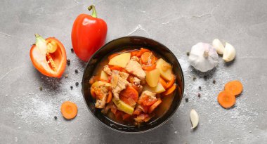 Bir kase lezzetli sığır güveci ve gri arka planda farklı malzemeler.