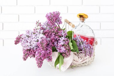 Tuğla duvarın yanındaki beyaz masada likör ve leylak dolu sepet.