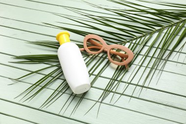 Güneş kremi şişeli güneş gözlüğü ve yeşil ahşap arka planda palmiye yaprağı.