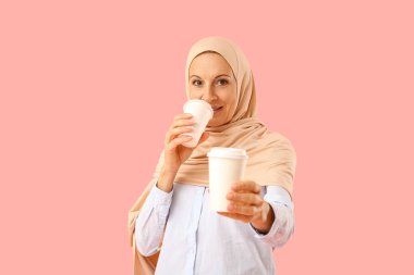 Pembe arka planda bir fincan kahveyle tesettürlü olgun Müslüman kadın