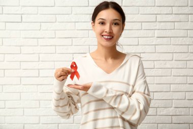 Beyaz tuğla duvarın yanında kırmızı kurdeleli güzel bir kadın. Dünya AIDS Günü konsepti
