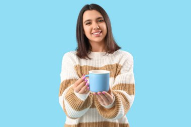 Mavi arka planda bir fincan çayı olan genç bir kadın.