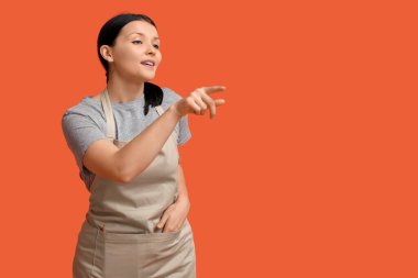 Güzel genç garson turuncu arka plandaki bir şeyi işaret ediyor.