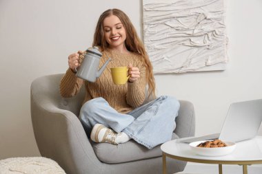 Genç bir kadın evdeki koltukta fincana çay dolduruyor.