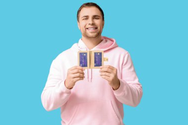 Cüzdanı mavi arka planda olan mutlu genç bir adam.