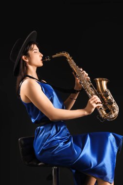 Güzel bir kadın karanlık arka planda saksafon çalıyor.