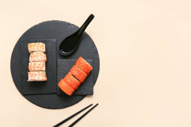 Lezzetli suşi ruloları, yemek çubukları ve bej arka planda kaşık.