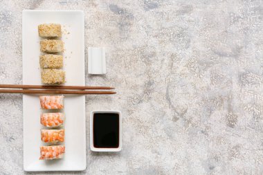 Gri grunge arka planda lezzetli suşi ruloları, yemek çubukları ve soya soslu tabak.