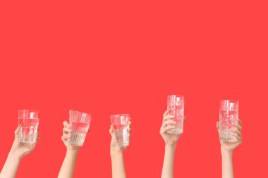 Kırmızı arka planda farklı su bardakları olan kadın eller.