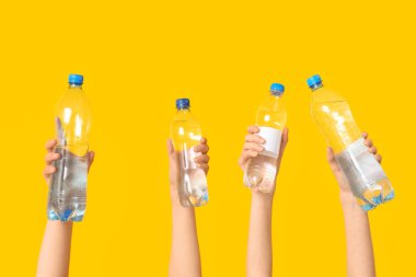 Sarı arka planda farklı su şişeleri olan kadın eller, yakın plan.