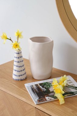 Narcissus çiçekli vazo ve dergi masada.