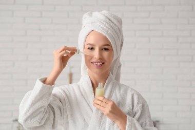 Güzel genç bir kadın banyoda pipetle yüzüne kozmetik yağı sürüyor.