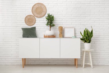 Beyaz tuğla duvarın yanında farklı dekorları olan beyaz ahşap dolap.