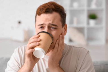 Genç adam kahve içiyor ve odadaki kanepede diş ağrısı çekiyor.