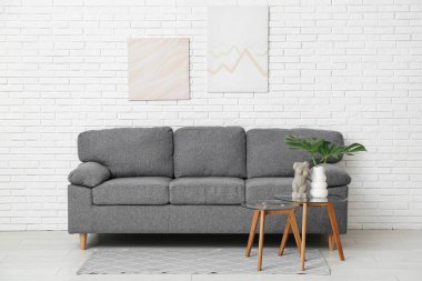 Beyaz tuğla duvarda asılı resim, rahat kanepe, kahve masası canavar yaprağı ve kadın figürlü oda.