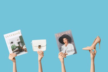 Farklı dergilere sahip kadın elleri, yüksek topuklu ve mavi arka planda şık bir çanta.