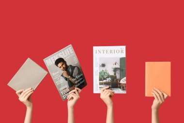 Farklı dergilere ve kırmızı arka planda kitaplara sahip kadın elleri