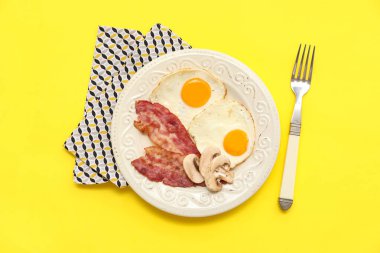 Sarı arka planda lezzetli kızarmış yumurta, pastırma ve mantar tabağı. Üst görünüm