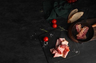 Tahtada pastırma dilimleri ve siyah arka planda kızarmış pastırma ile kızartma tavası. Üst görünüm