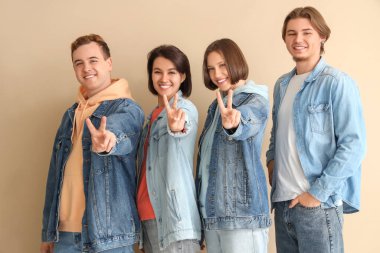 Kot elbiseli bir grup genç bej arka planda zafer jesti gösteriyor.
