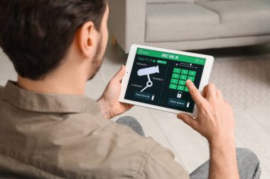 Genç adam odada akıllı ev güvenlik sistemi kontrol paneli kullanıyor, yakın plan.