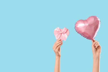 Kalp şeklinde balonu ve mavi arka planda hediye kutusu olan kadın elleri. Sevgililer Günü kutlaması