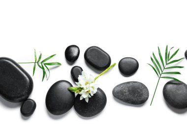 Siyah spa taşlı kompozisyon, güzel çiçekler ve beyaz arka planda palmiye yaprağı.