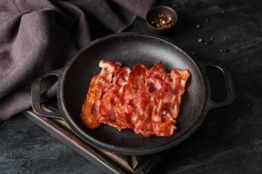 Kızarmış pastırmalı tava ve siyah arka planda bir kase biberli mısır.