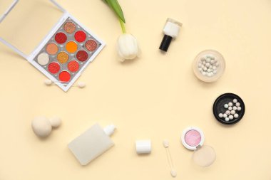 Çerçeve, parfüm, makyaj ürünleri, aksesuarlar ve bej arkaplandaki çiçekten yapılmıştır.