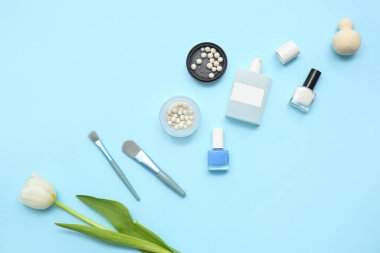 Makyaj ürünleri, oje, parfüm şişesi ve mavi arka planda çiçekler.