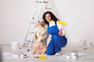 Memlekette tamirat sırasında üniformalı, sevimli bir Avustralyalı çoban köpeği olan mutlu Afro-Amerikan ressam kadın.