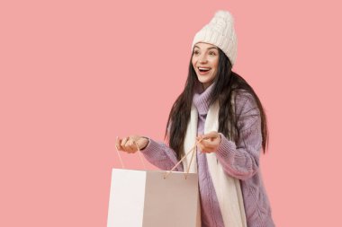 Pembe arka planda alışveriş çantası olan kalın elbiseli güzel bir kadın.