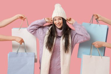 Pembe arka planda alışveriş torbaları olan kalın elbiseli ve elleri olan güzel genç bir kadın.