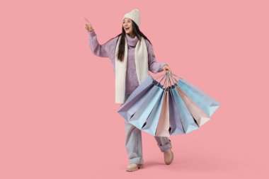 Pembe arka planda alışveriş torbaları olan kalın giysili güzel bir kadın.