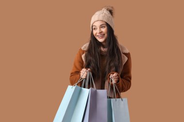 Kahverengi arka planda alışveriş torbaları olan kalın elbiseli güzel bir kadın.
