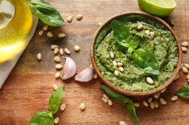 Tahtada fesleğen yaprağı, çam fıstığı ve sarımsak olan bir kase lezzetli pesto sosu.