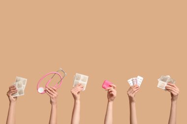 Hardal alçılı kadın elleri, ilaç kutusu, steteskop ve bej arka planda haplar.