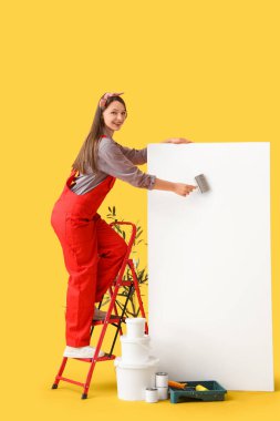Genç bayan ressam sarı arka planda boş bir posterle resim yapıyor.