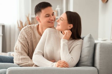 Evdeki kanepede sıcak kazaklar içinde kucaklaşan sevimli genç çift.