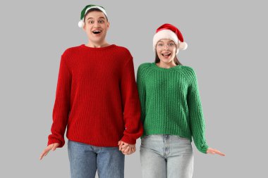 Sıcak süveter ve gri arka planda Noel Baba şapkası giyen mutlu genç çift.