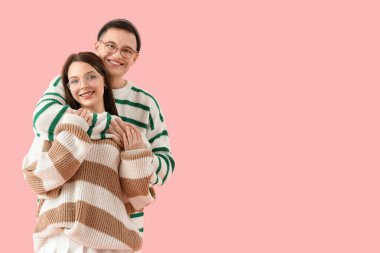 Pembe arka planda sıcak kazak giyen şık genç bir çift.