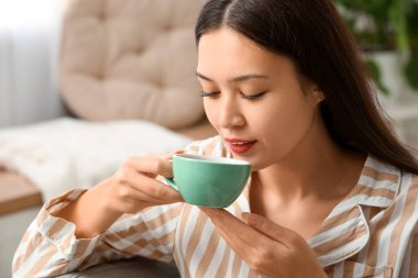 Güzel genç Asyalı kadın oturma odasında sıcak çay içiyor.