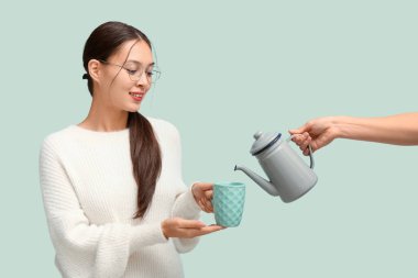 Güzel genç Asyalı kadın elinde çay fincanı ve elinde çaydanlıkla mavi arka planda.