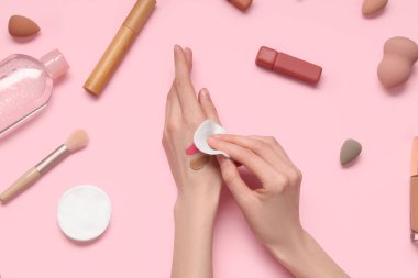 Pamuk yastıklı kadın elleri ve pembe arka planda farklı dekoratif kozmetikler.