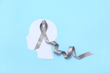 Mavi arka planda gri farkındalık kurdelesi olan kağıt insan kafası. Beyin kanseri kavramı