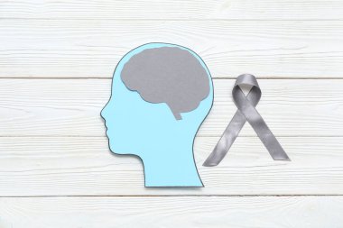 Beyni olan kağıt insan kafası ve beyaz ahşap arka planda gri farkındalık kurdelesi. Kanser kavramı