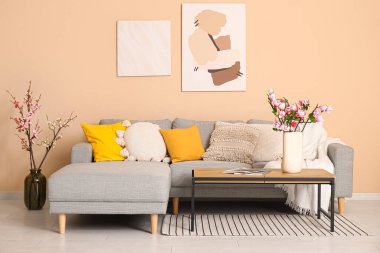 Konforlu kanepe, kahve masası ve oturma odasının içinde çiçek açan bahar dalları.