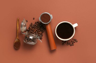 Bir fincan sıcak kahve ve kahverengi arka planda toz bulunan portafilter.