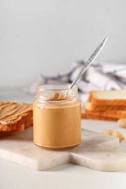 Fıstık ezmesi kavanozu ve beyaz arka planda kaşık ve tost.